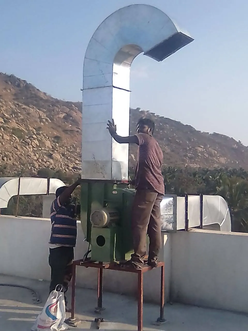 Two technicians installing a rooftop blower unit and discharge duct